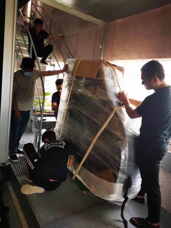 Moving crew maneuvering a wrapped upright piano on a stair landing