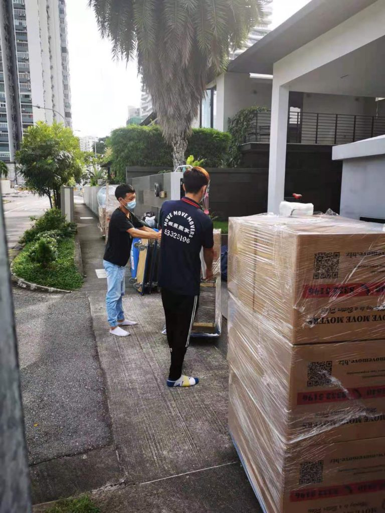 Two Move Move Movers crew members with a trolley and wrapped cartons outside a gate