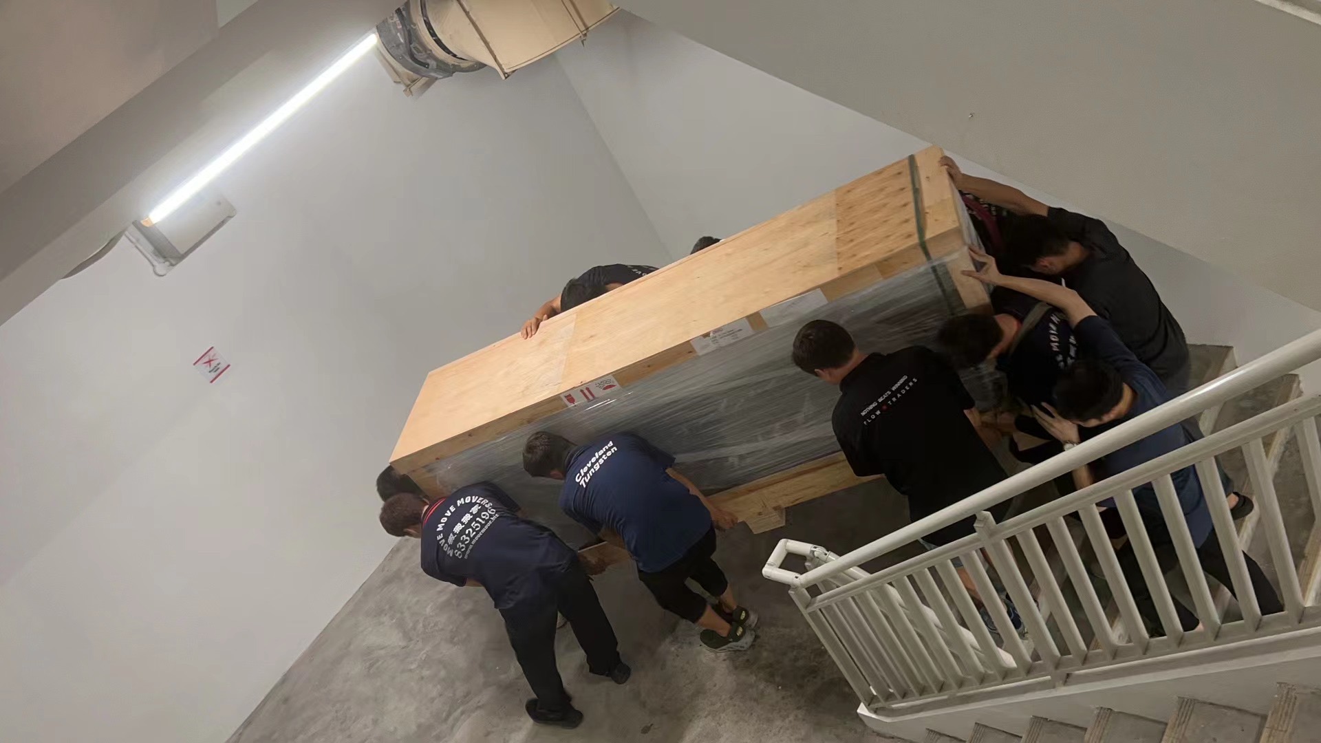 Move Move Movers crew carrying a large crated item through a commercial stairwell