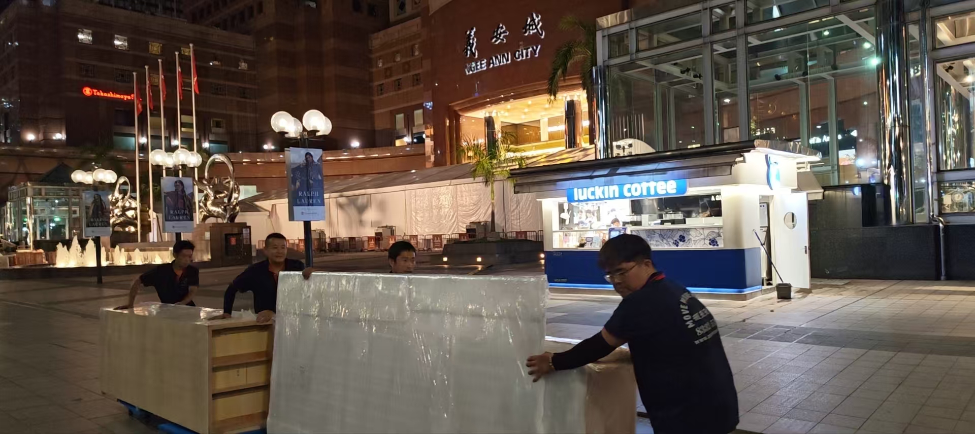 Crew moving wrapped counter units at night near Ngee Ann City in Singapore