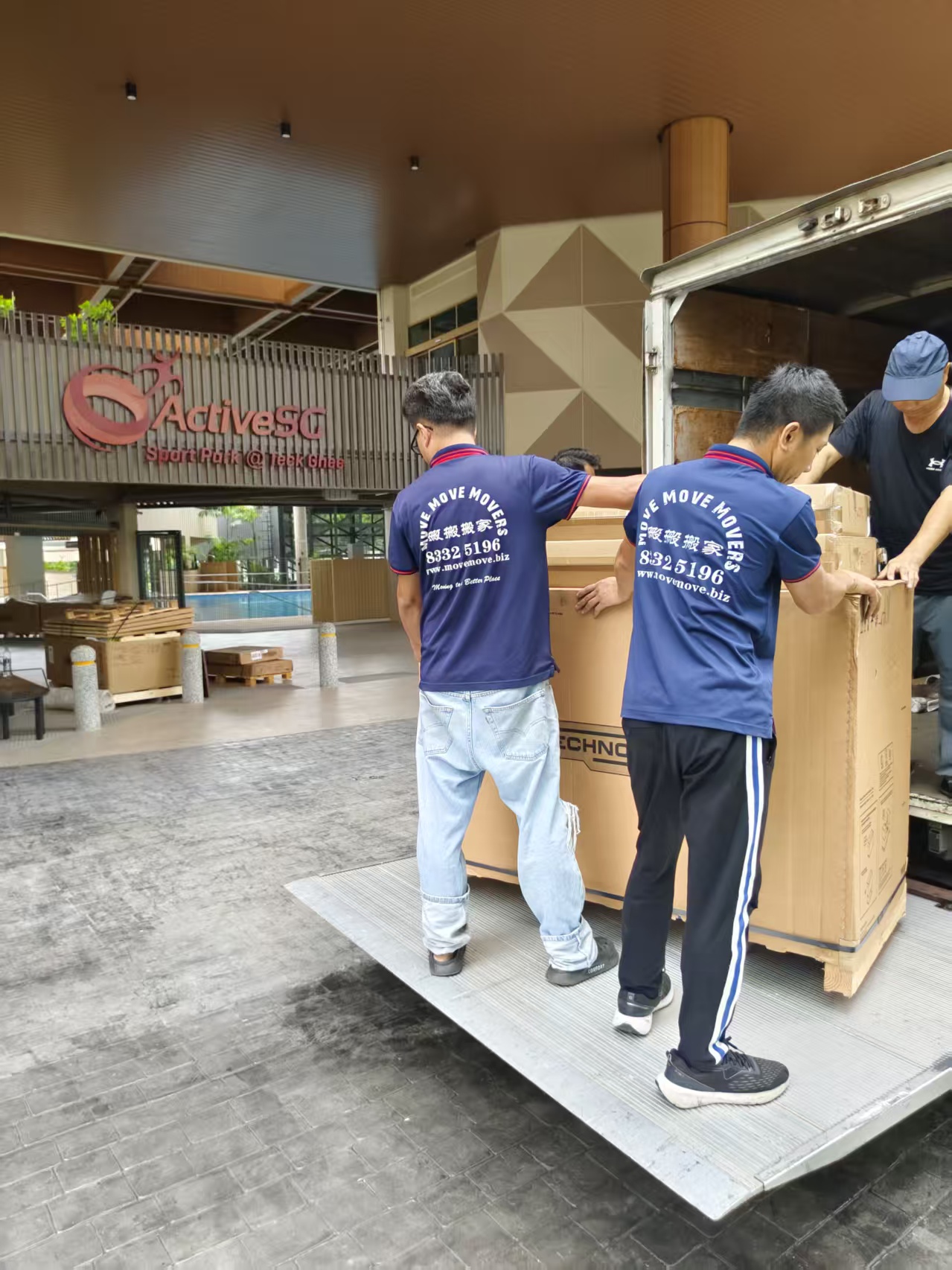 Two movers and a supervisor guiding a crated unit on a truck tail lift