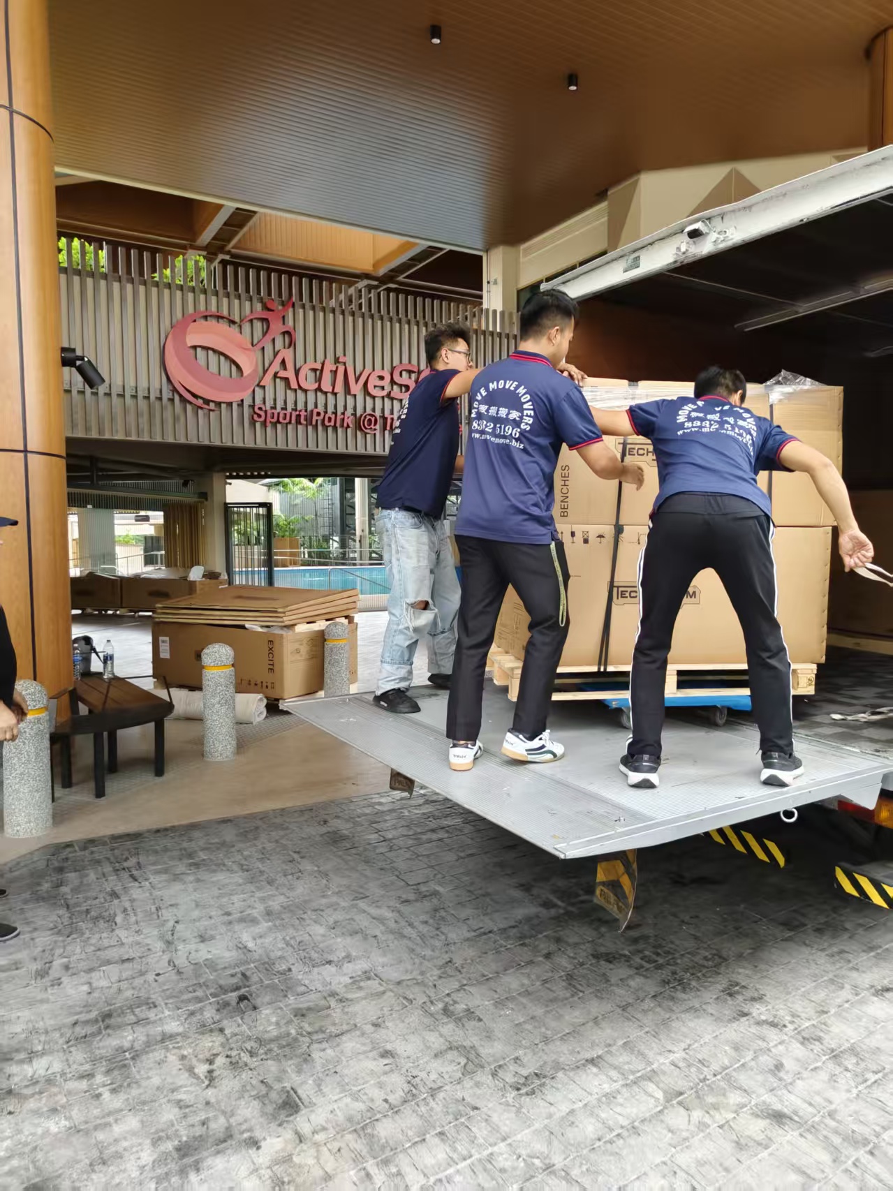 Three movers loading large boxed gym equipment into a truck at ActiveSG Teck Ghee