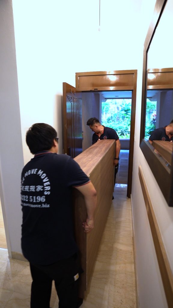 Move Move Movers crew carrying a tall wooden panel through a narrow corridor