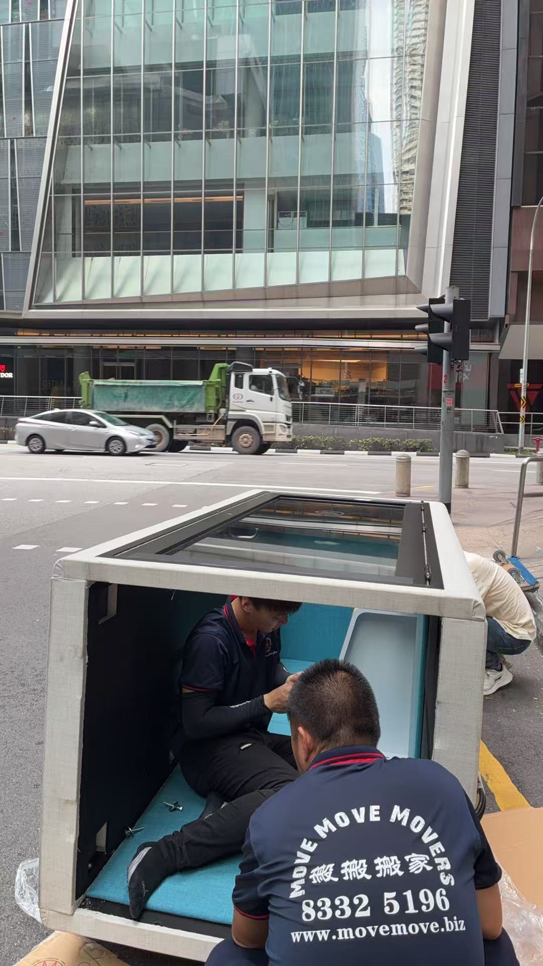 Move Move Movers staff loading a large glass-fronted item into a moving truck on a Singapore street