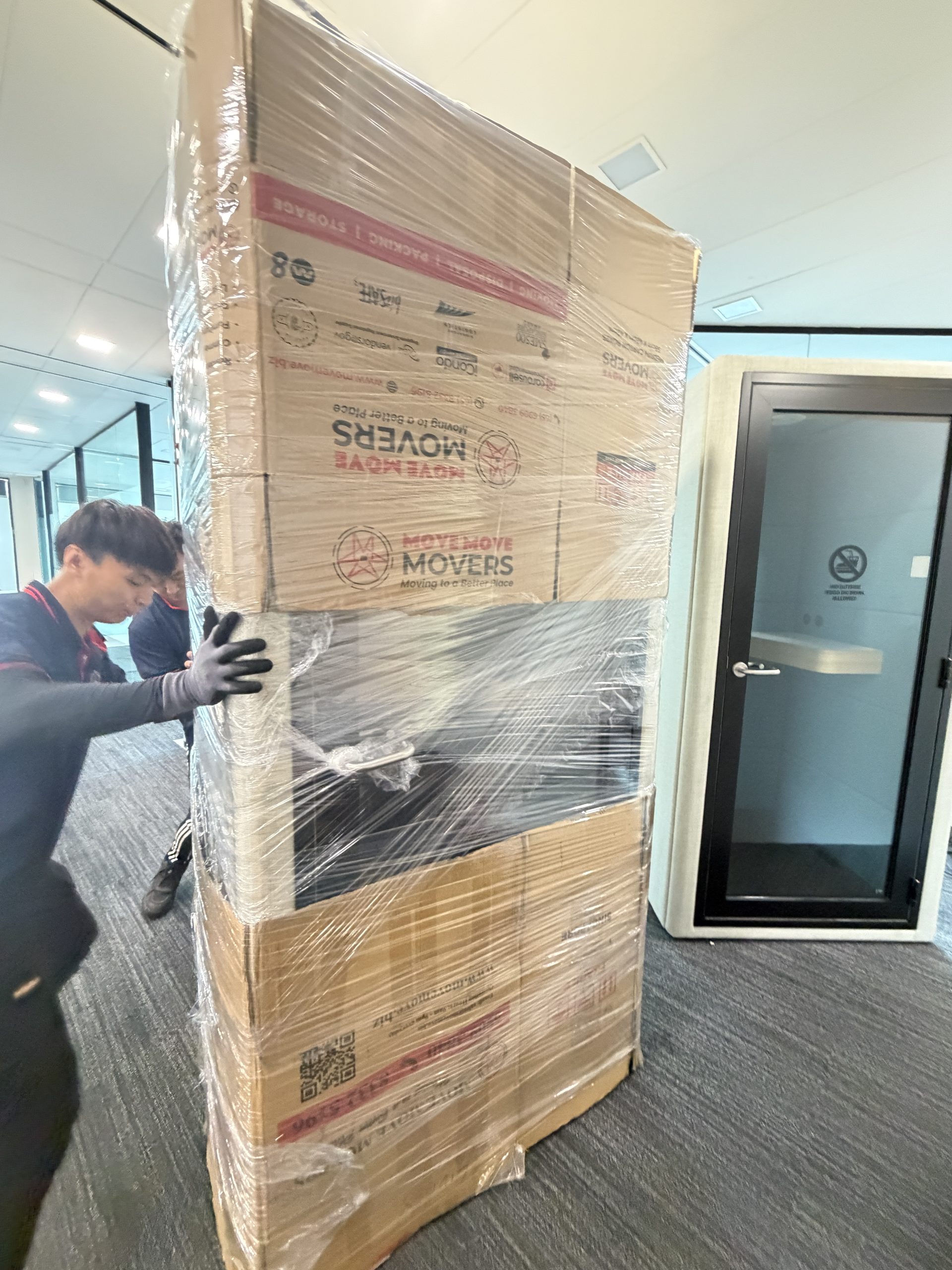 Move Move Movers staff pushing a tall wrapped office crate through an indoor hallway in Singapore