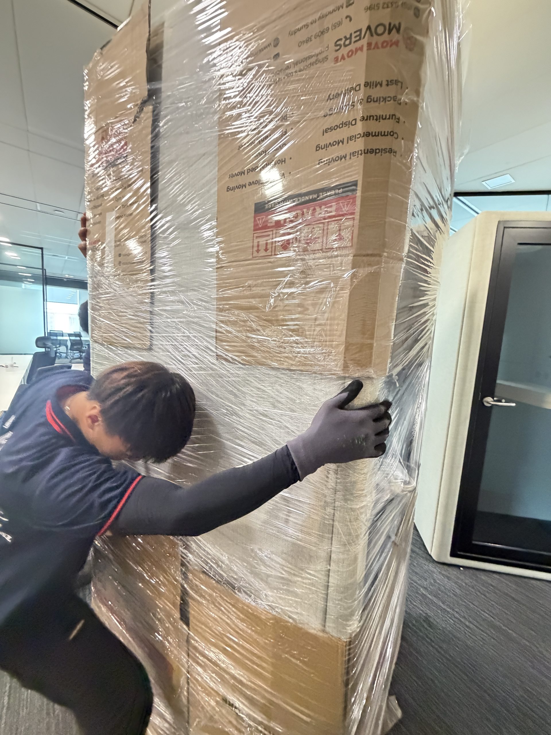 Two Move Move Movers staff pushing a tall wrapped crate through an office hallway in Singapore