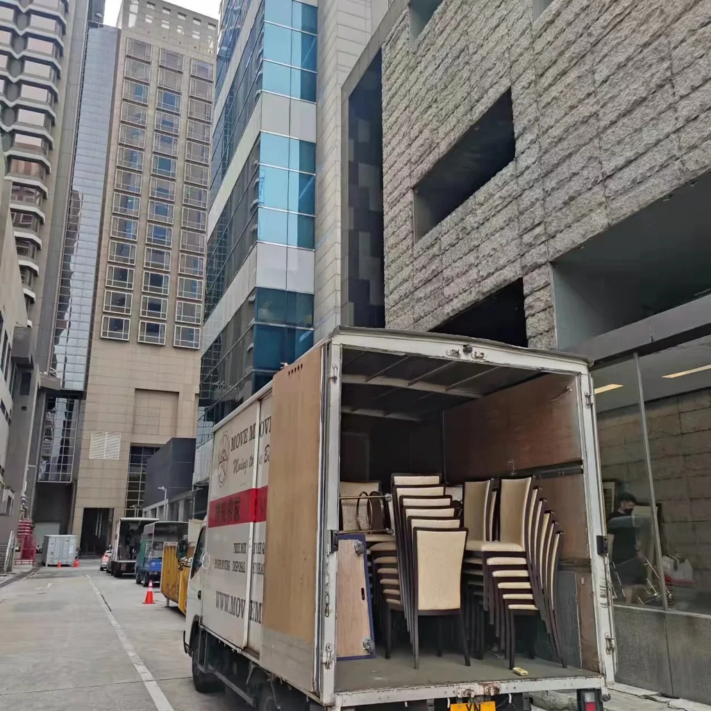 Stacked office chairs loaded inside a Move Move Movers lorry at a commercial building