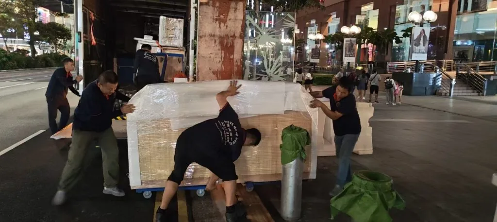 Move Move Movers crew pushing a large wrapped cabinet across an outdoor plaza
